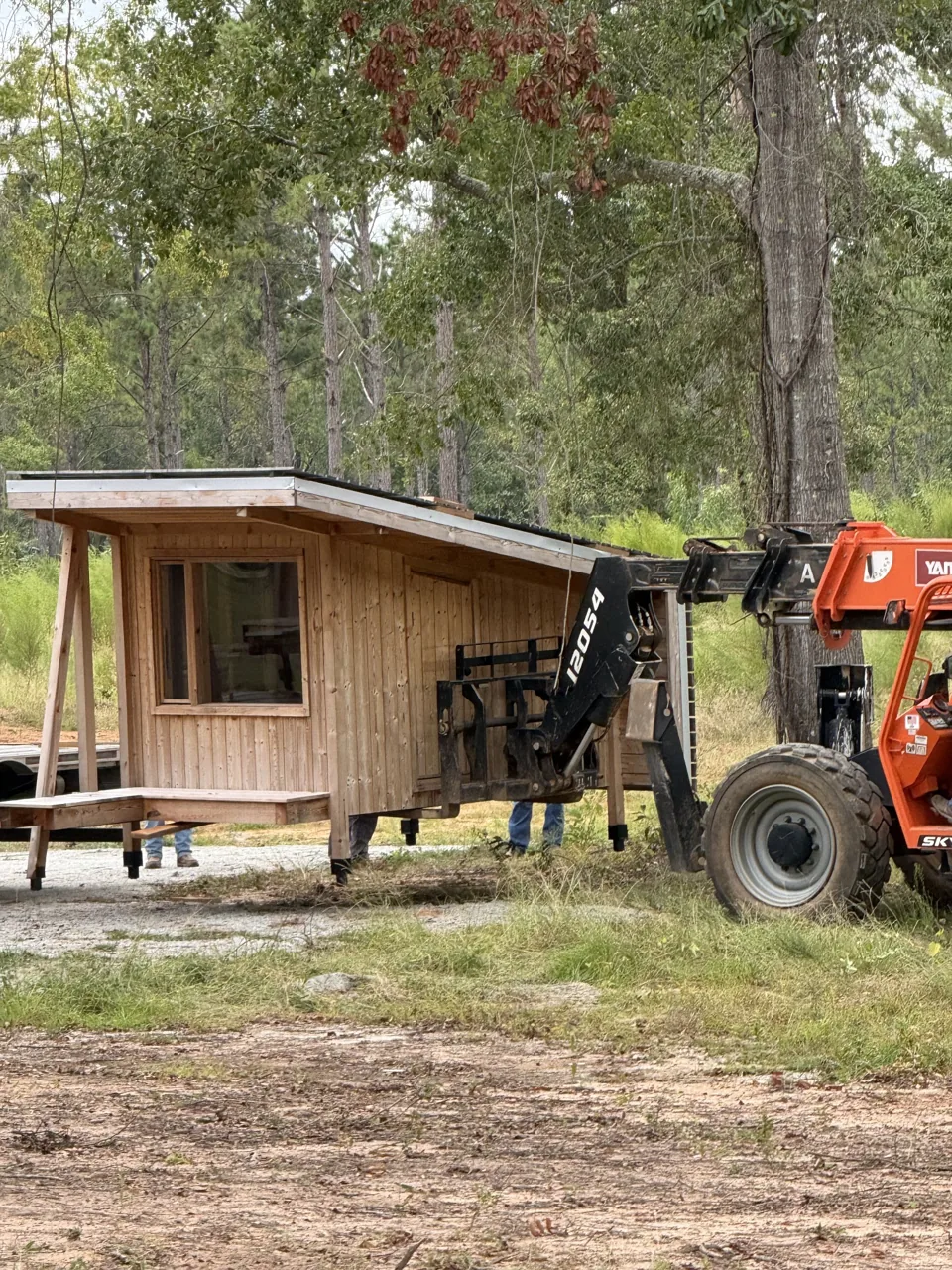 A timber cabin being positioned among trees at Clay Cosmos
